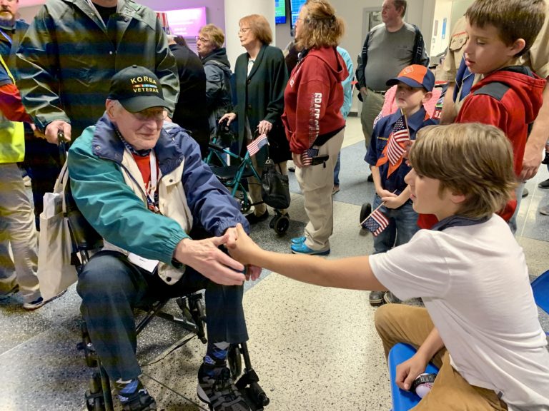 Young boy shaking a veteran's hand on Honor Flight to show respect